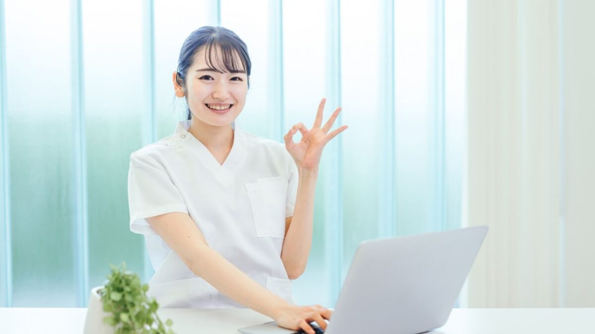 RECRUIT-歯科助手- 女性がパソコンの前に座って指でOKサインを出している