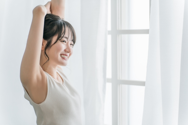 寝起きにカーテンの前で朝日を浴びる女性 