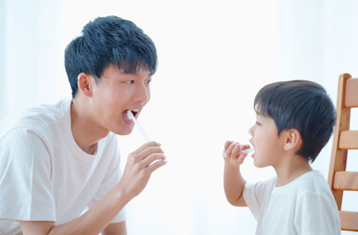 供の歯磨き習慣を教える父親と楽しそうに磨く男の子のイメージ